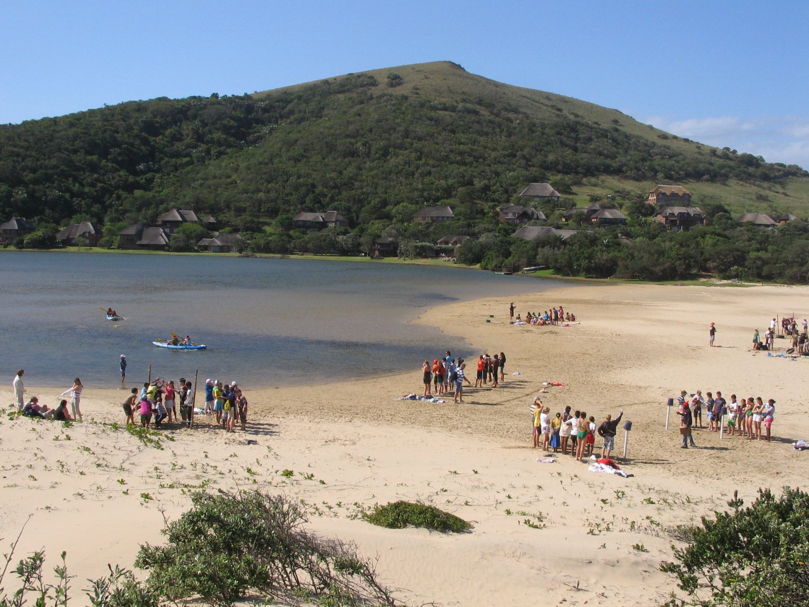 School group on the beach at the Cefani lagoon with the resort's thatched chalets behind